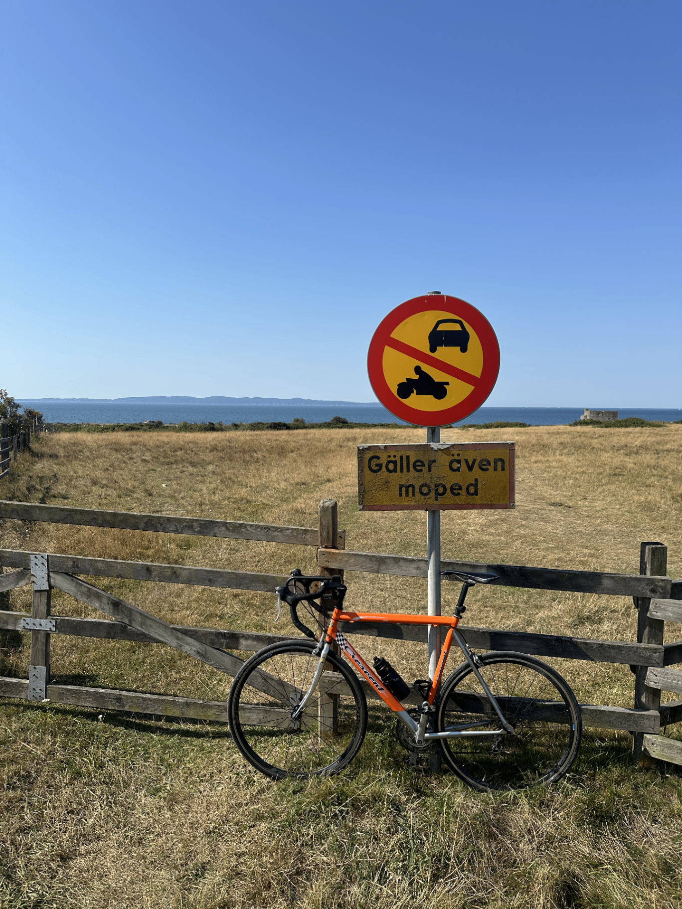Min orangea racer cykel lutad mot ett staket vid havet, under en skylt som säger att mopeder inte får köra här.