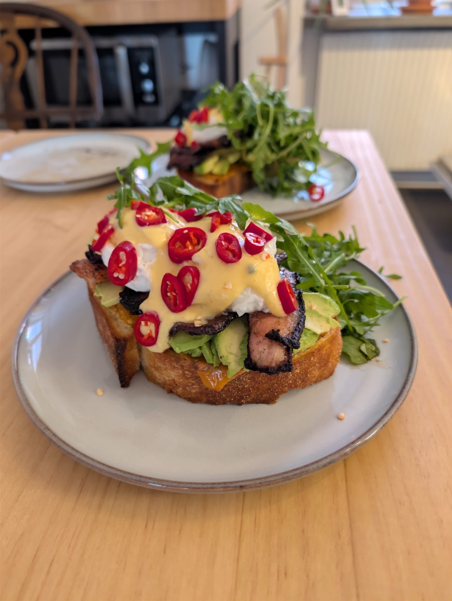 Hemlagad brunch på rostat bröd med avokado, bacon, ägg och hollandaisesås, toppat med röd chili och rucola.